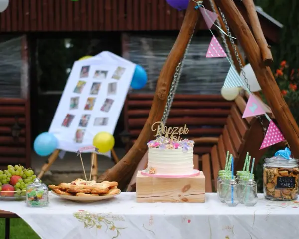 Na stole na roczek kładzie się tort, owoce, ciasteczka i słodkości. Dekoracje tworzą girlandy i zdjęcia.