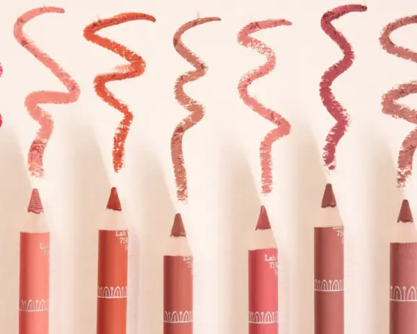 Plusieurs crayons à lèvres de différentes teintes, avec des échantillons de leur utilisation en traits ondulés.
