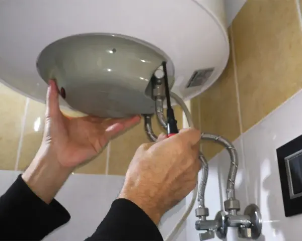 Mani che effettuano la manutenzione dello scaldabagno elettrico, avvitando una vite con un cacciavite.