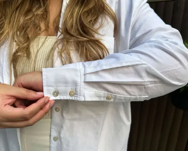 Sotto una camicia bianca, un top a coste color crema. Dettagli sui polsini con gemelli.