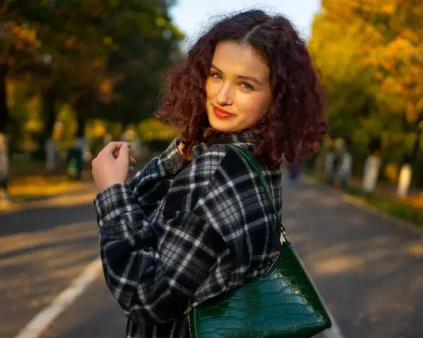 Dziewczyna w kratę, co to za styl? Ciepła flanela i zielona torebka na tle jesiennego parku.