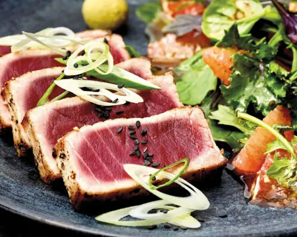 Tataki de atún perfectamente sellado, servido con una ensalada fresca de cítricos y hojas verdes.