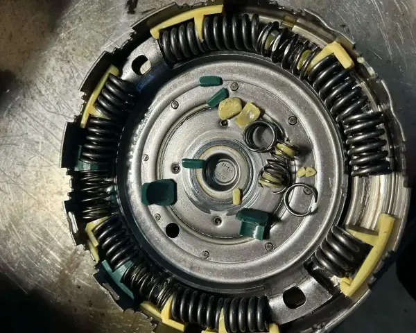 Zużyte elementy sprzęgła powershift: połamane zielone wkładki i sprężyny, objawy zużycia widoczne na metalowych częściach.