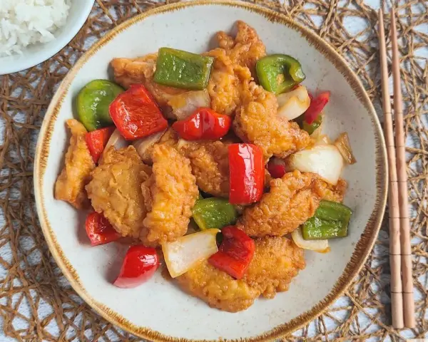 Delicioso pollo agridulce con pimientos rojos y verdes, y cebolla. Un plato vibrante y sabroso, listo para disfrutar.