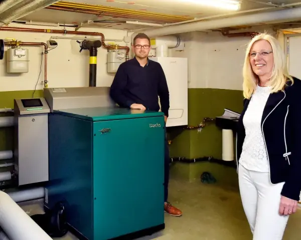 Mann und Frau stehen neben einem grünen Nano BHKW-Gerät in einem Heizungsraum.