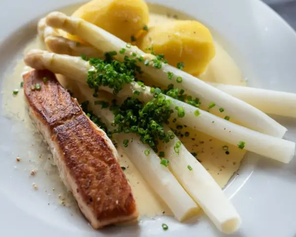 Ein Stück Lachs mit Spargel, Kartoffeln und Sauce Hollandaise. Der Spargel ist mit Schnittlauch bestreut.