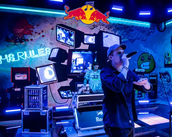 Jan rapowanie koncert w neonowym świetle. Na ścianie napisy "VHS RULES", logo Red Bulla i stare monitory.