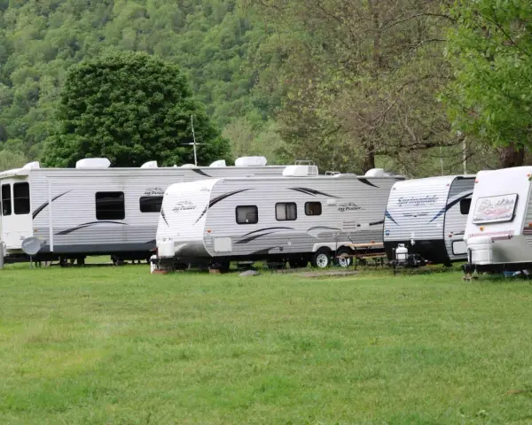 Rząd przyczep kempingowych na zielonej trawie, w tle las. Idealne miejsce na camping Górna Wetlinka.