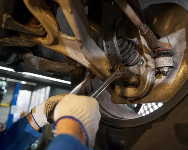 Mechanik dokręca śrubę w zawieszeniu samochodu. Widać elementy układu kierowniczego i amortyzator.