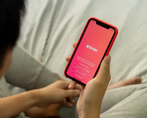 Osoba trzyma telefon z aplikacją Tinder. Zastanawiasz się, czy warto założyć Tindera? Może to początek nowej znajomości.