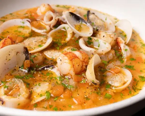 Sopa de mariscos con gambas, calamares y almejas en un caldo dorado con perejil.