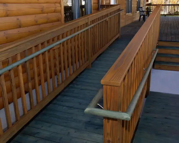 A wooden wheelchair ramp with railings curves around a log cabin. This shows how to build a wheelchair ramp for accessibility.