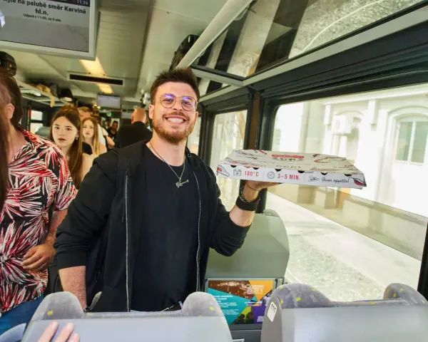 Uśmiechnięty mężczyzna z pizzą w ręku w pociągu relacji Kraków-Praga.
