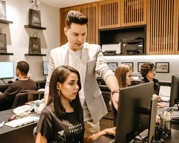 Koordynator w jasnej marynarce wskazuje coś na monitorze pracownicy.