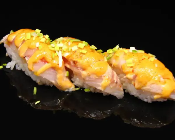 Trzy kawałki sushi z rybą i kremowym sosem, posypane szczypiorkiem. Idealne na lekki posiłek, gdy zastanawiasz się nad sushi kalorie.