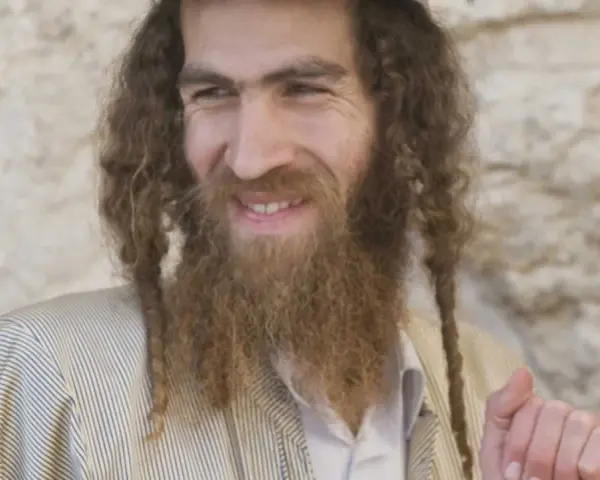 A smiling man with long, curly hair and a beard, wearing traditional Jewish attire. His appearance sparks curiosity about what ethnicity was Jesus.
