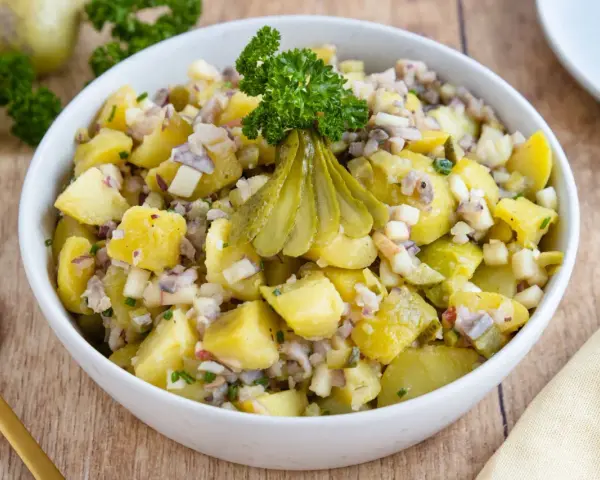 Schlesischer Kartoffelsalat mit Gurken, Zwiebeln und Petersilie, appetitlich garniert.