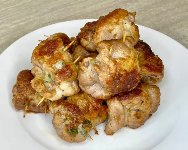 Un mucchio di bombette pugliesi ricetta, dorate e succulente, tenute insieme da stuzzicadenti, su un piatto bianco.