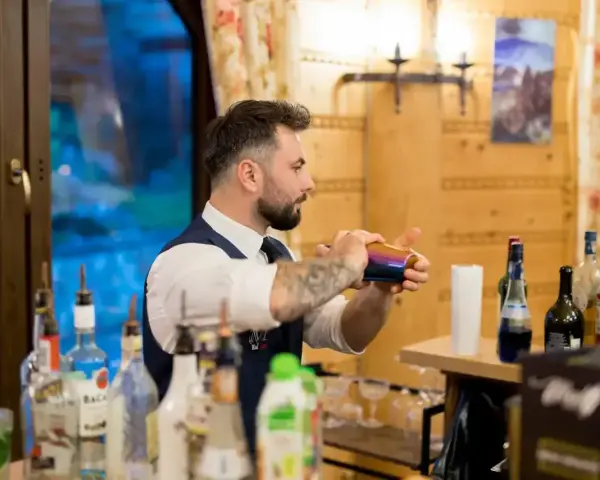Barman na wesele cena: profesjonalista miesza drinki za barem, otoczony butelkami alkoholu i dekoracjami.