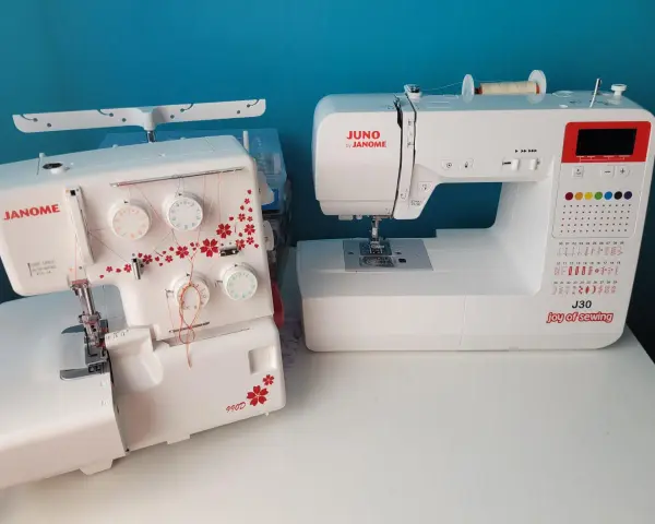 Dwie maszyny do szycia: biały owerlok Janome 990d z czerwonymi kwiatami i biała maszyna Juno by Janome J30.