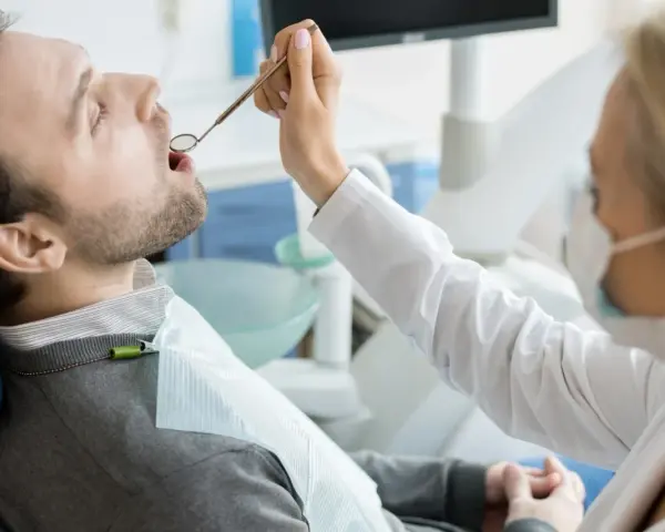 Pacjent u dentysty, zastanawia się, ile kosztuje wizyta u dentysty prywatnie. Lekarz bada jego zęby.