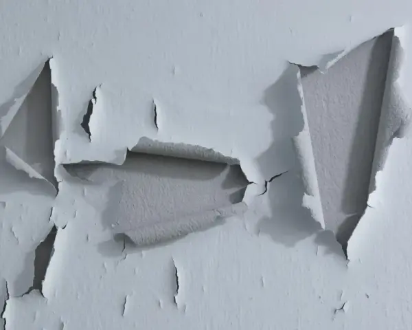 Pintura desconchada revela capas de color gris bajo la superficie blanca.
