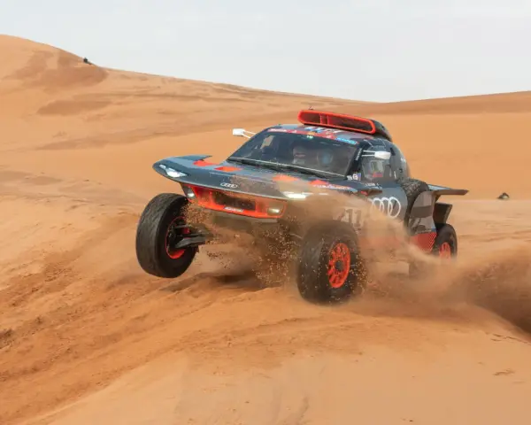 Un'auto da rally Audi sfreccia tra le dune, sollevando sabbia. Un'emozionante tappa del percorso Parigi-Dakar.