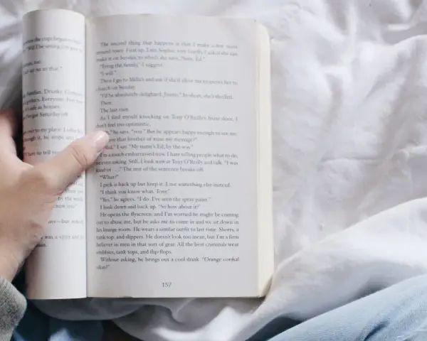 Mano sosteniendo un libro abierto con relatos cortos para mujeres. La página muestra texto y el número 157.