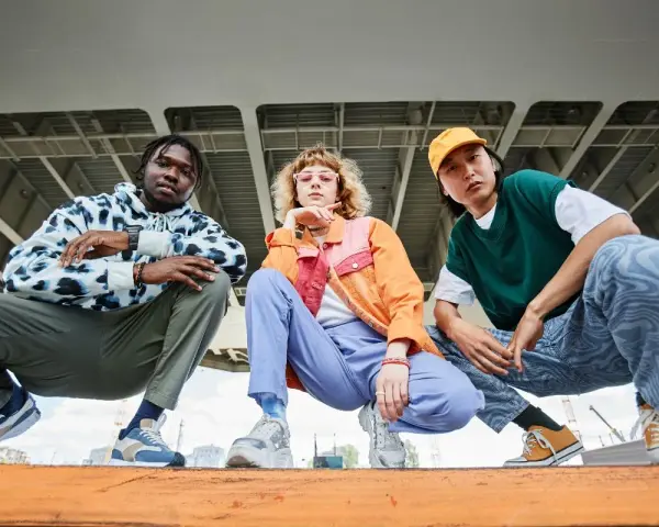 Tre giovani con look urbani, ognuno con le sue sneakers, mostrano cosa sono le sneakers: calzature comode e alla moda per ogni stile.