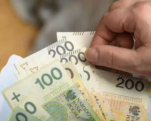 Dłoń trzyma banknoty 100 i 200 zł. Czy to już zapowiedź podwyżki najniższej krajowej 2026?