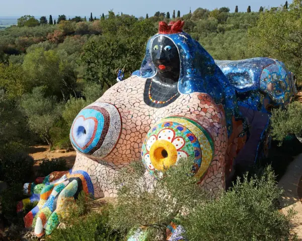 Œuvres d'art de Niki de Saint Phalle : une sculpture monumentale et colorée, représentant une femme allongée, ornée de mosaïques vives, dans un paysage verdoyant.