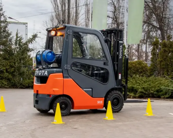 Pomarańczowo-szary wózek widłowy Toyota z butlą gazową, otoczony żółtymi pachołkami, gotowy do testów UDT.