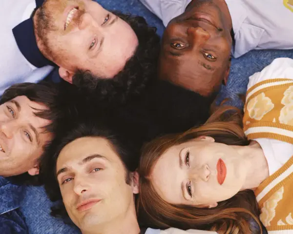 Les membres de Metronomy, cinq visages souriants, forment une étoile sur un fond bleu.