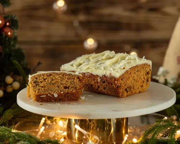 Pyszny, wilgotny naked cake marchewkowy z kremem i wiórkami białej czekolady, udekorowany świątecznymi światełkami i gałązkami choinki.
