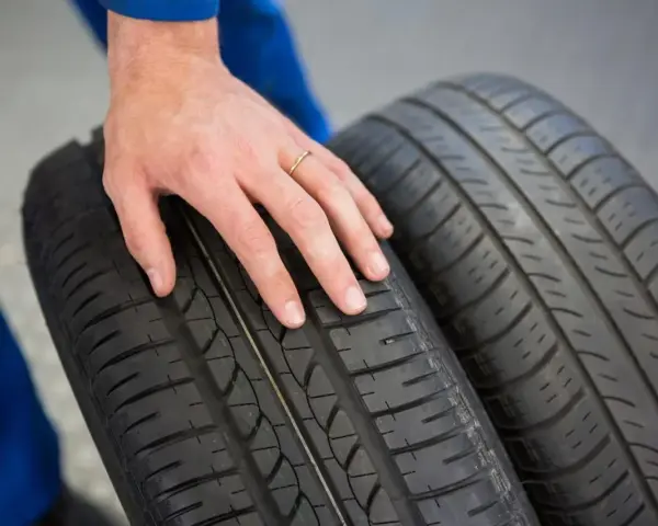 Dłoń mechanika dotyka bieżnika opony Hankook, sprawdzając jej stan. Dobre opony Hankook opinie to podstawa bezpiecznej jazdy.