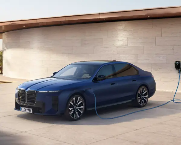 Elegancka, granatowa BMW hybryda podłączona do ładowarki przy nowoczesnym domu z widokiem na morze.