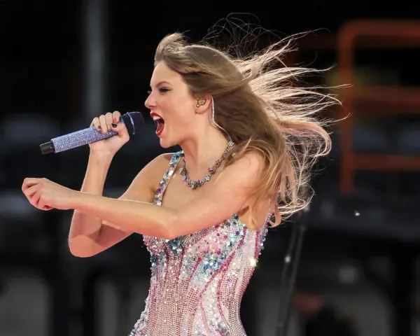 Taylor Swift w błyszczącej sukience śpiewa na koncercie w Warszawie, włosy rozwiane przez wiatr.