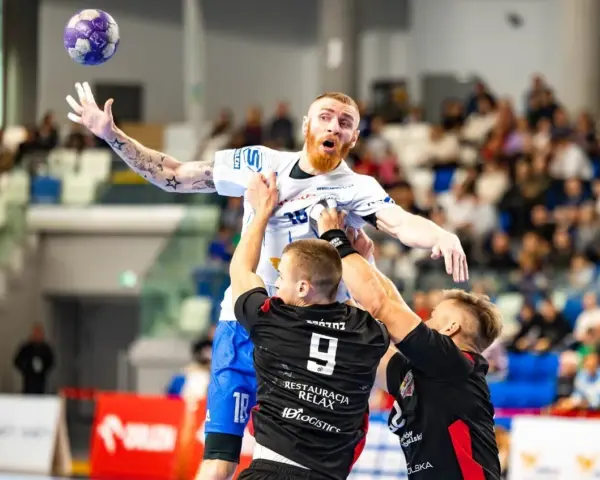 Jakub Wolski w akcji, walczy o piłkę w powietrzu z dwoma przeciwnikami.