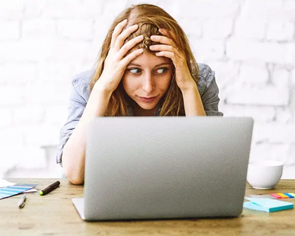 Verzweifelte Frau mit Händen in den Haaren, die auf einen Laptop starrt. Die Website-Migration scheint sie zu überfordern.