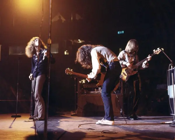 Energetyczny **Led Zeppelin koncert** na scenie. Wokalista z burzą włosów, gitarzysta pochylony nad instrumentem, basista grający w tle.