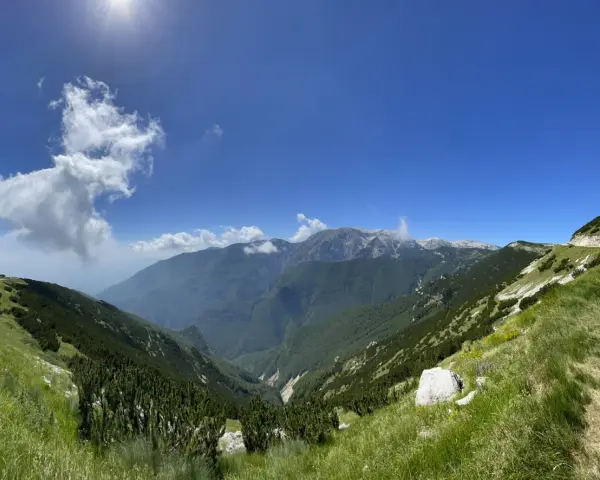 Panoramica mozzafiato sui monti dell'Abruzzo, con un sentiero che sale verso un **block house** e torri di trasmissione.