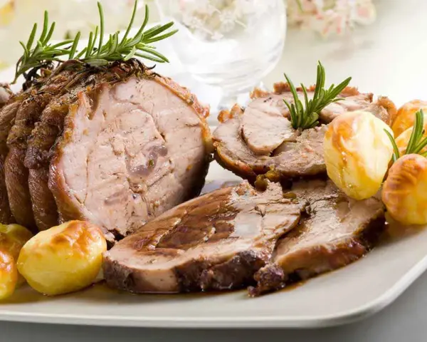 Succulento arrosto di vitello affettato, guarnito con rosmarino e accompagnato da patate arrosto dorate.