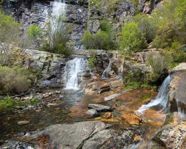 Las chorreras de despeñalagua, cascadas de agua blanca cayendo sobre rocas rojizas y verdes arbustos en un paisaje rocoso.