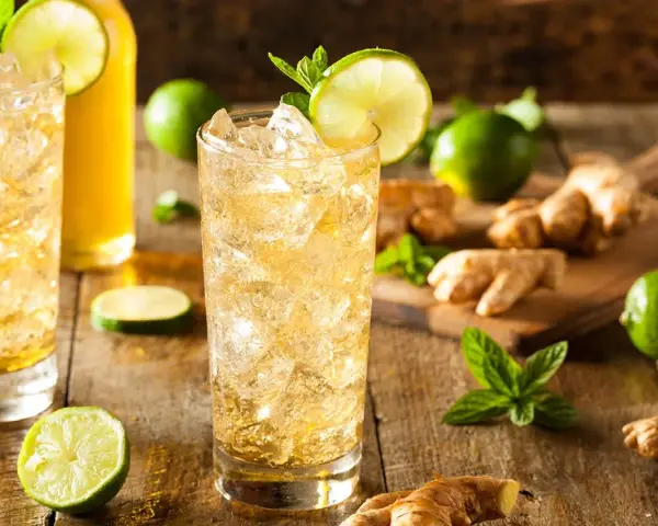 En uppfriskande ginger beer drink med is, lime och mynta. Ingredienser som ingefära och lime ligger utspridda.
