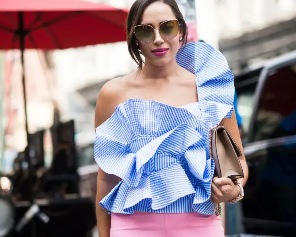 Eleganza in **abbinamento rosa e blu**: top a balze a righe azzurre e bianche con pantaloni rosa cipria, occhiali da sole e borsa a tracolla.