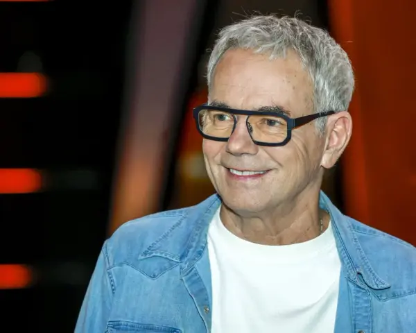 Uśmiechnięty mężczyzna w okularach, w jeansowej koszuli, jakby czekał na pytanie: "Jaka to melodia?".