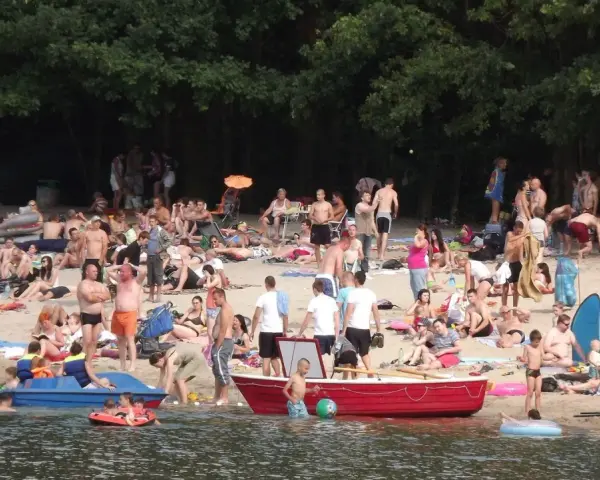 Tłum ludzi odpoczywa na plaży nad jeziorem w Jelczu Laskowicach. Słońce, piasek i woda tworzą idealne warunki do letniego relaksu.