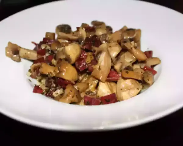 Champiñones salteados con trocitos de jamón, servidos en un plato blanco. Un plato sencillo y sabroso.