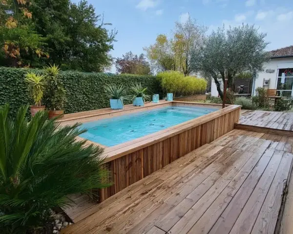 Aménagement abord piscine hors sol en bois, avec terrasse et végétation luxuriante.