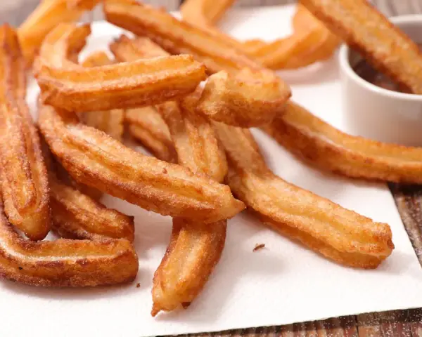 Goldbraune Churros, frisch frittiert, mit Zucker bestreut. Ein Churro wird in eine Schüssel mit Schokoladensauce getunkt. Ein echtes Churros Rezept Original.